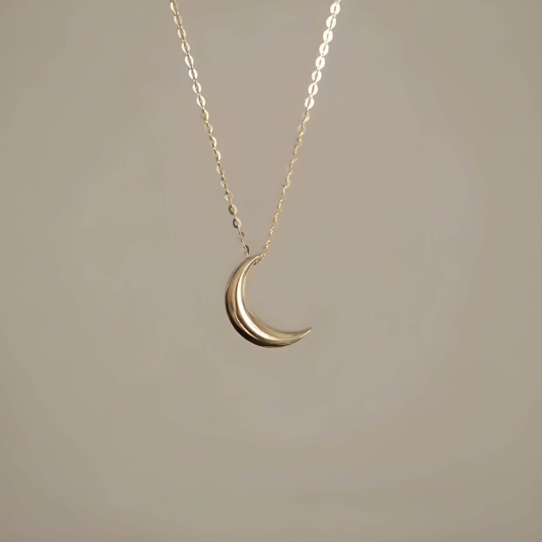 Gold crescent moon necklace on a thin chain against a beige background