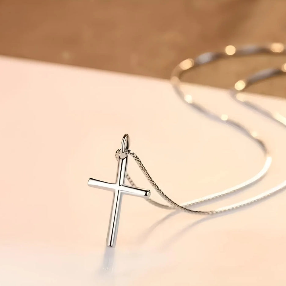 Silver cross pendant on a chain against a soft beige background