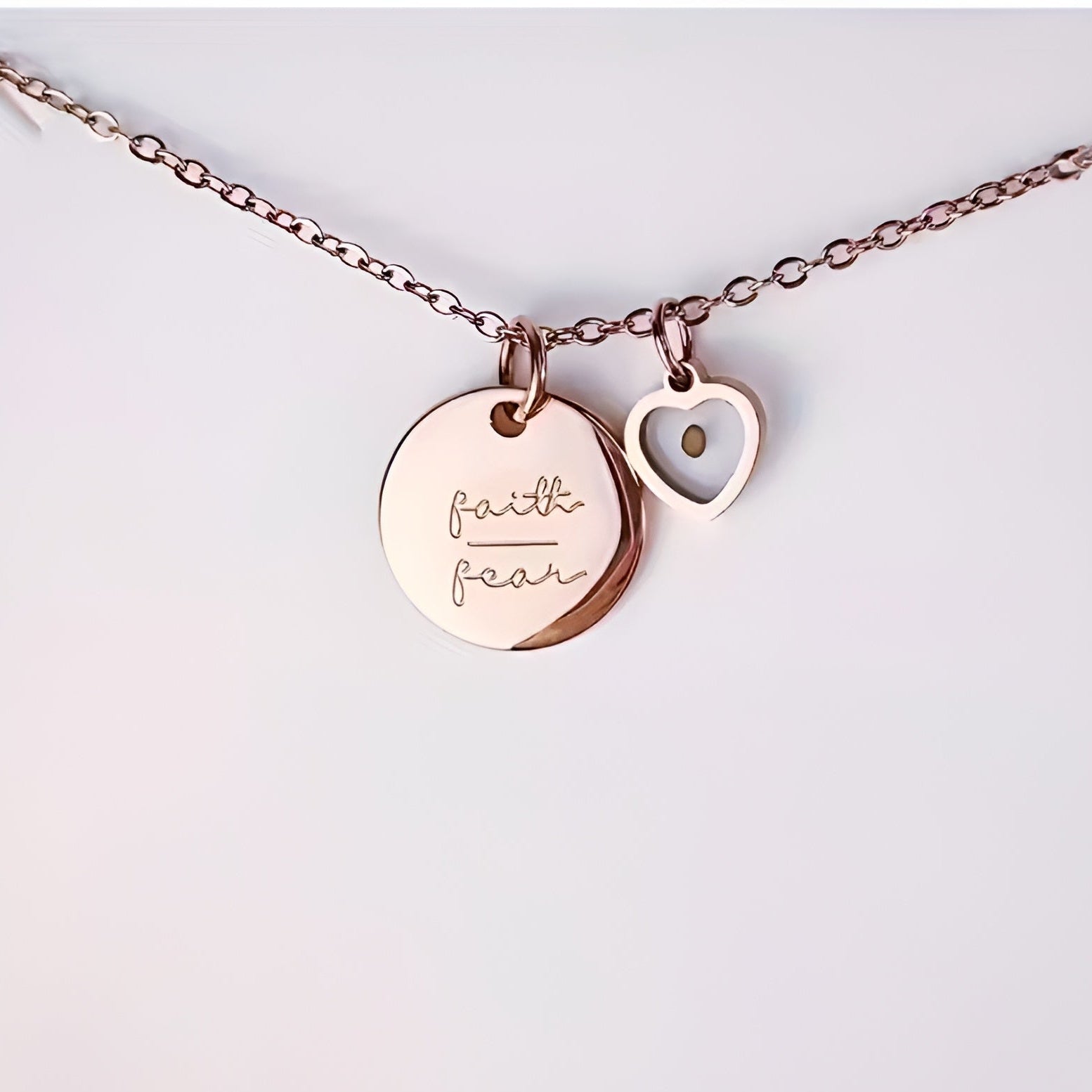 Rose gold necklace with 'faith' and 'heart' charms on a light gray background