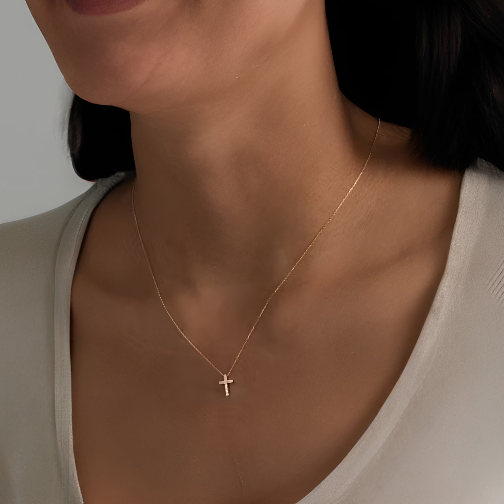 Gold necklace with a small cross pendant on a neutral background. Elegant gold cross pendant for women.