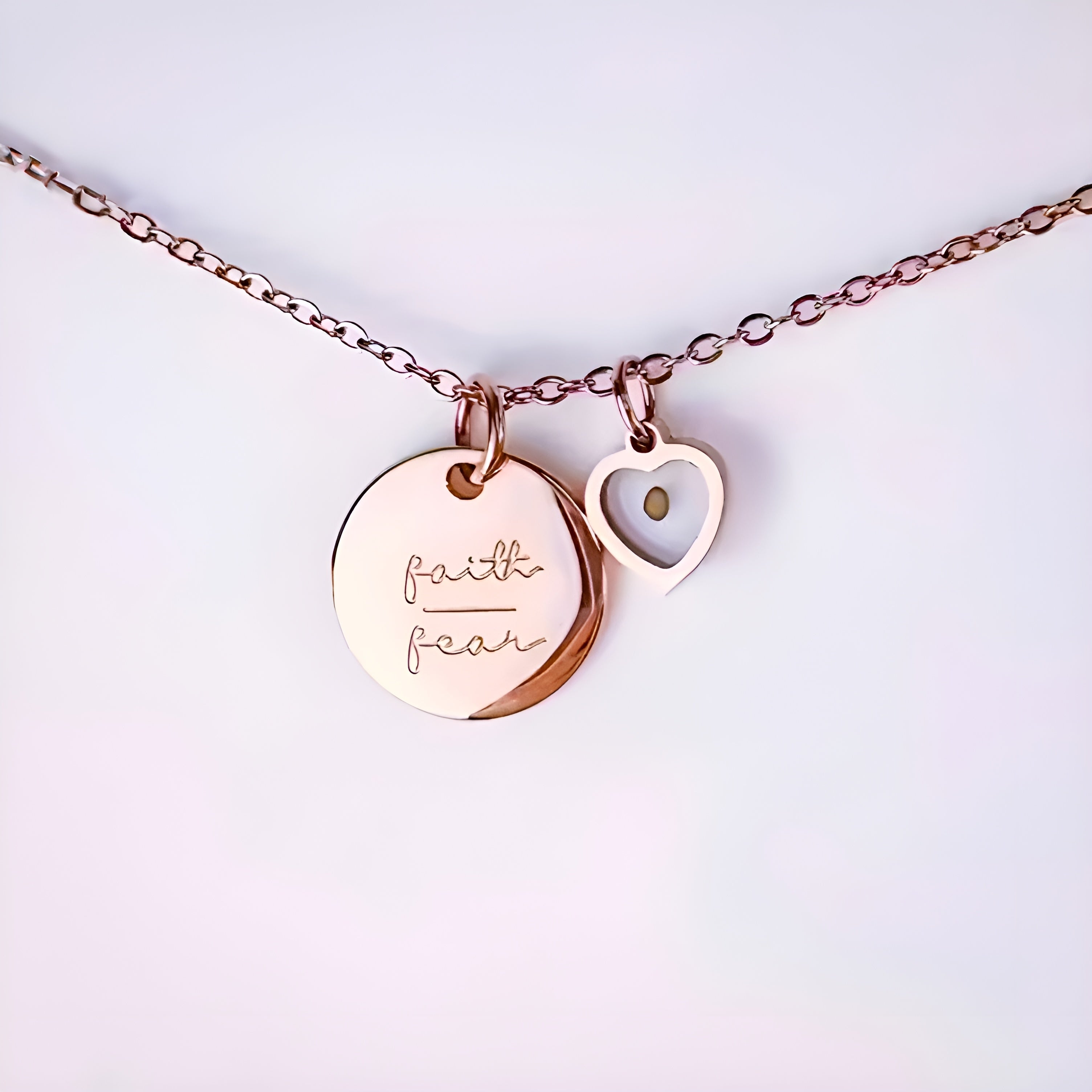 Rose gold necklace with two heart-shaped pendants on a light pink background saying Faith Over Fear.