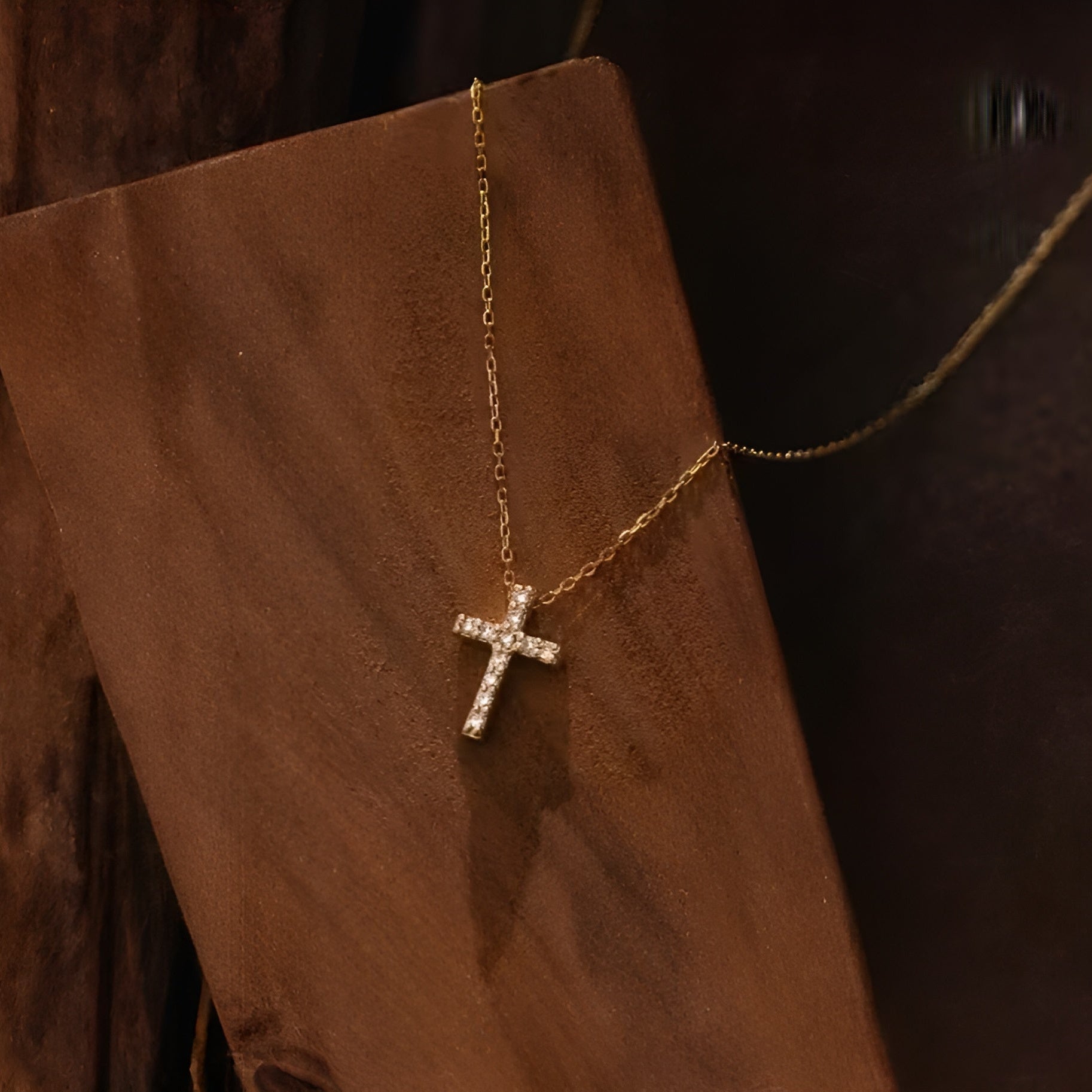 Gold cross necklace on a brown textured surface. Minimalist Christian necklace with adjustable chain.
