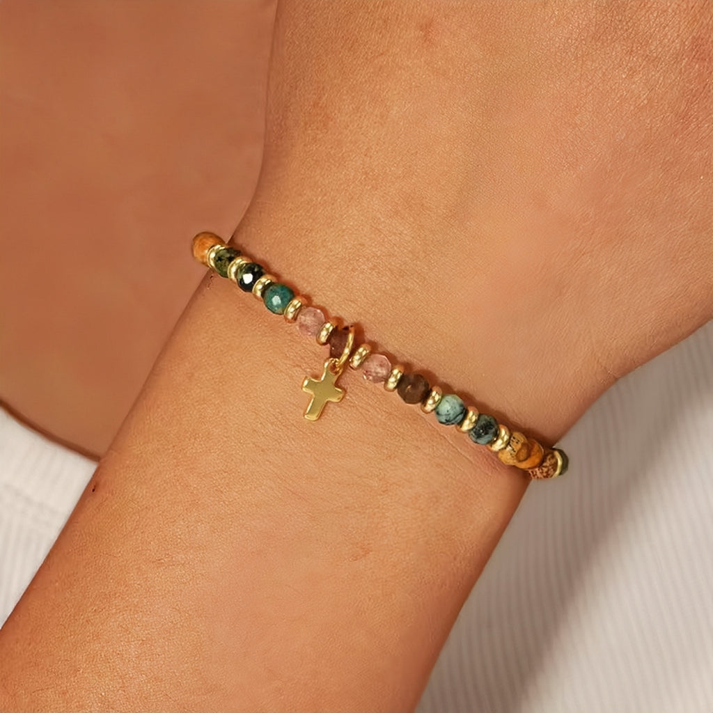 Bracelet with colorful beads and a gold cross charm on a wrist against a neutral background