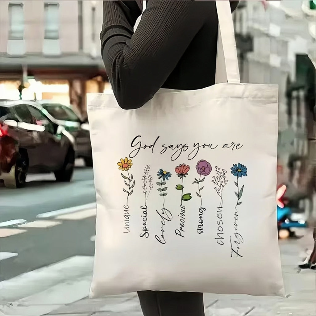 Tote bag with motivational text and floral designs held by a person on a city street.