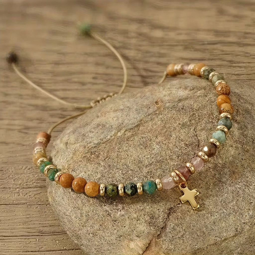 Beaded bracelet with a cross charm on a stone surface