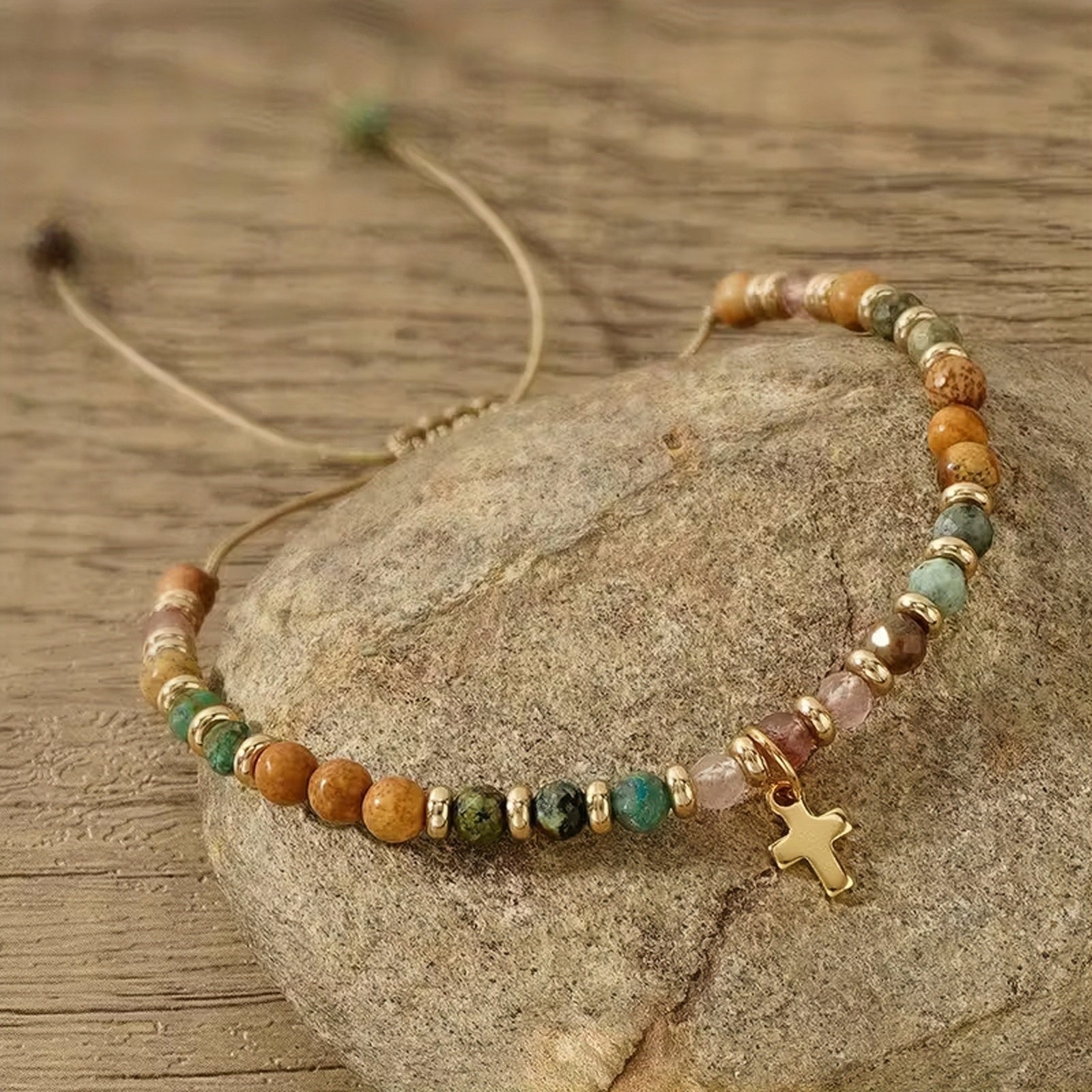 Beaded bracelet with a cross charm on a stone surface