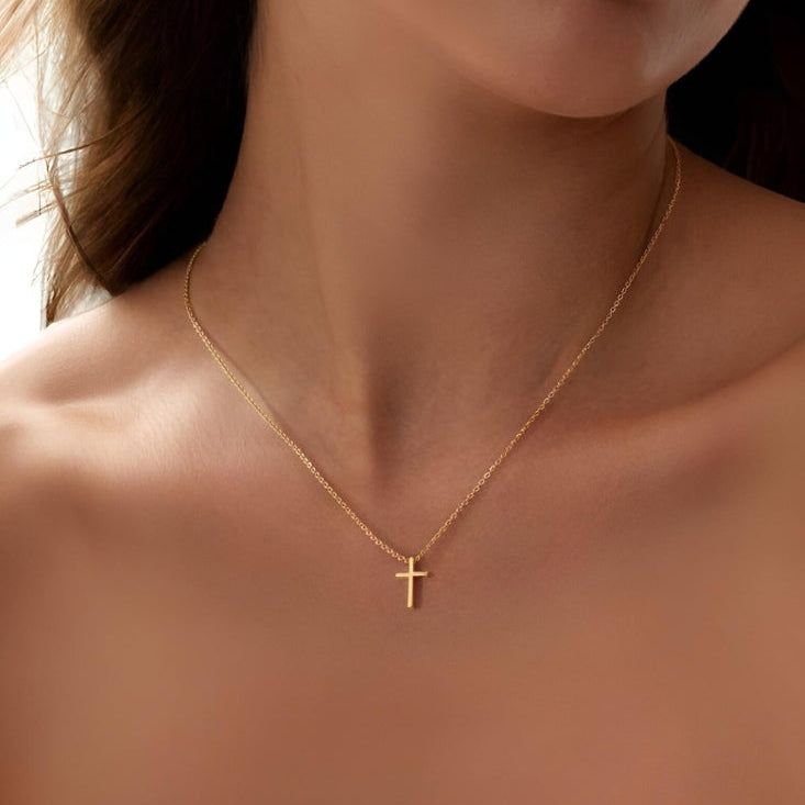 Gold necklace with a cross pendant on a person's neck against a neutral background