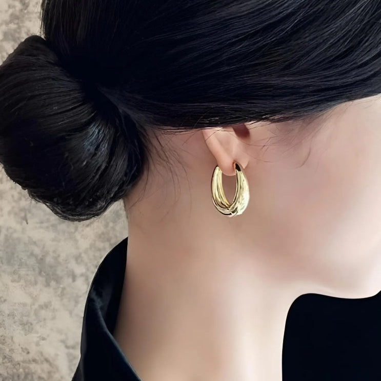 Gold hoop earring worn by a person with dark hair tied back.