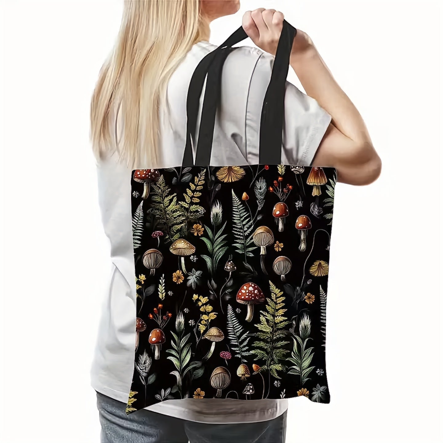 Person holding a tote bag with a nature-themed design featuring mushrooms and plants on a black background.