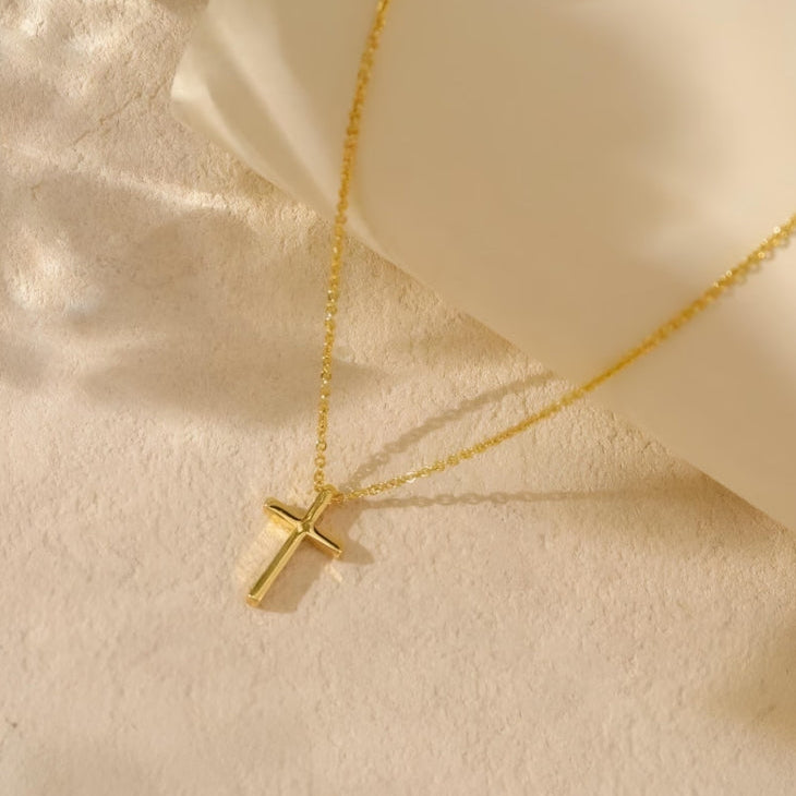 Gold cross necklace on a beige fabric background