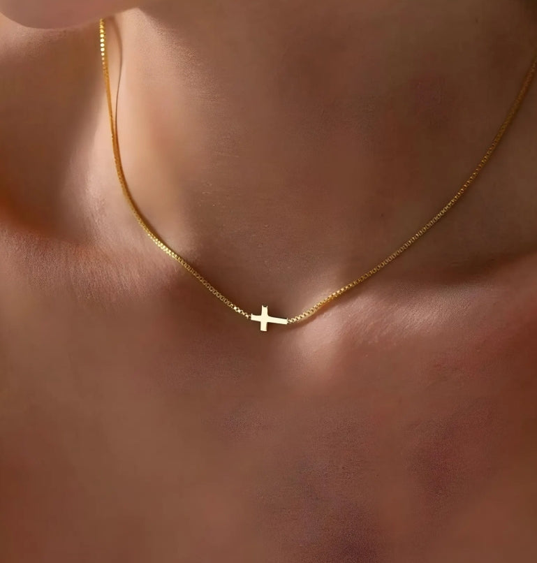 Gold cross necklace with a cross pendant on a person's neck against a neutral background