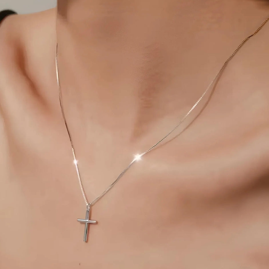 Silver cross necklace on a person's neck against a neutral background
