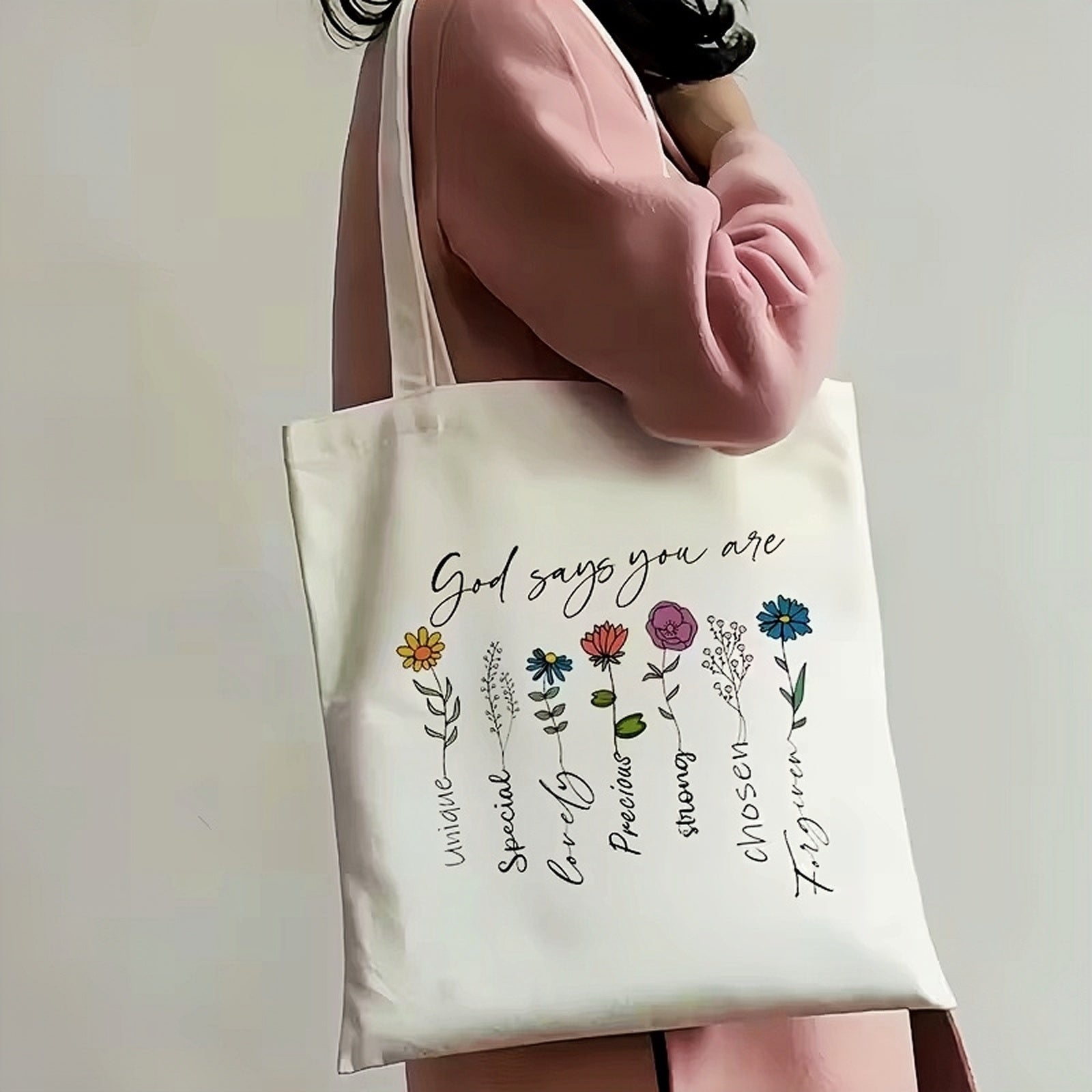 Tote bag with floral design 'god says you are' bag held by a person wearing a pink coat.