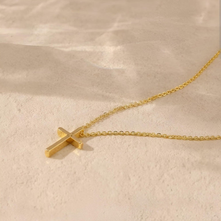 Gold cross necklace on a beige background