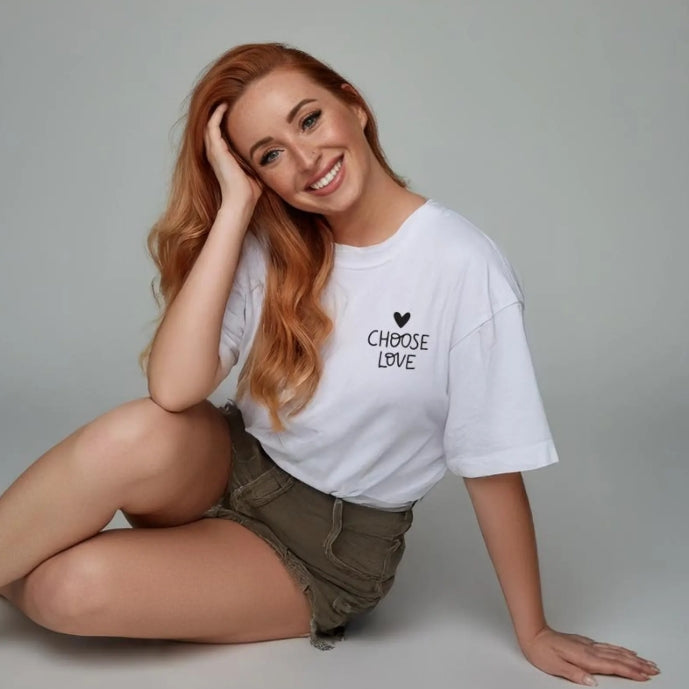 Woman wearing a white t-shirt with 'CHOOSE LOVE' text, sitting on a grey background, mental health awareness tee