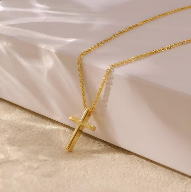 Gold cross necklace on a soft white surface