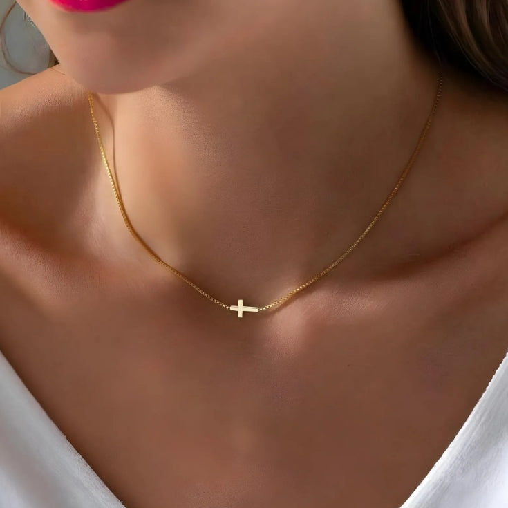 Gold cross necklace with a small cross pendant worn by a person.