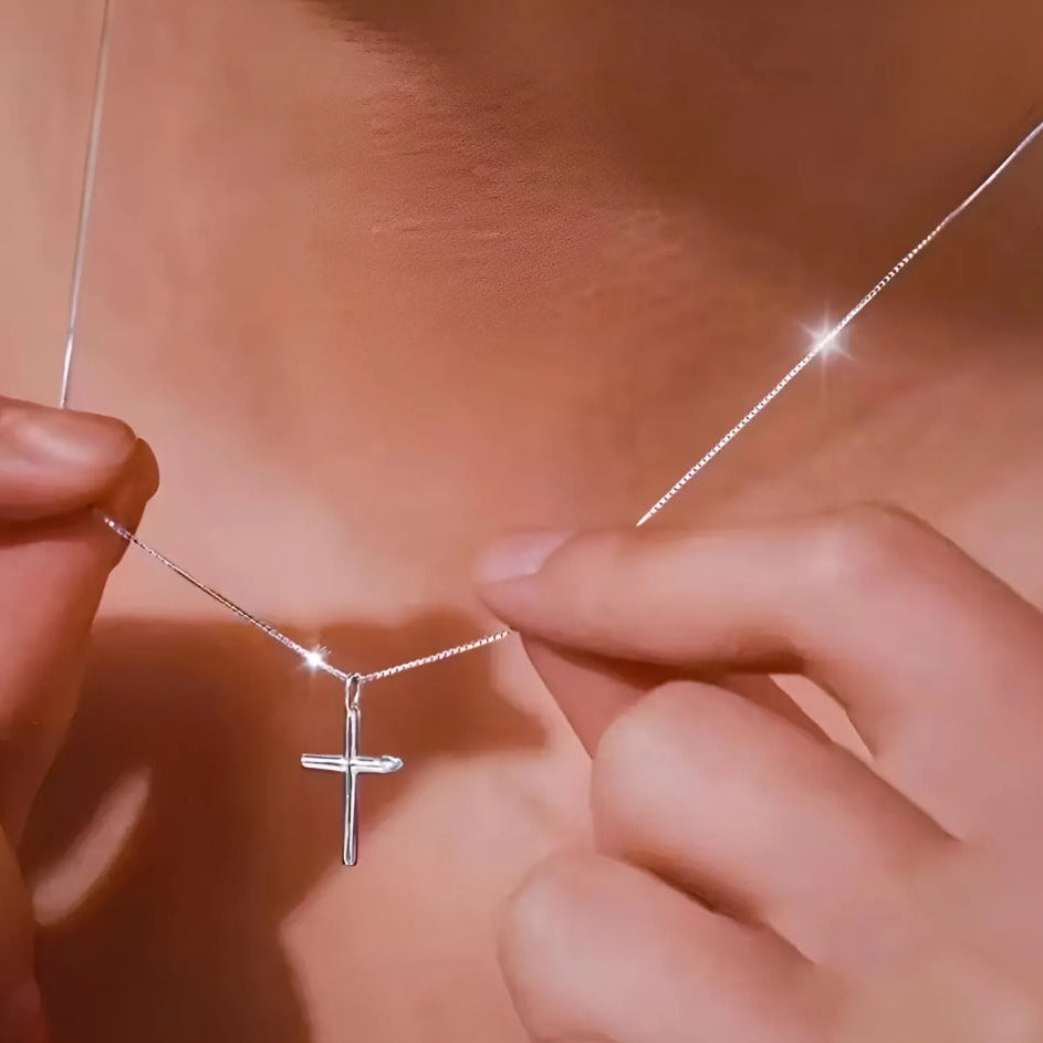 Silver cross necklace being held by hands against a blurred background