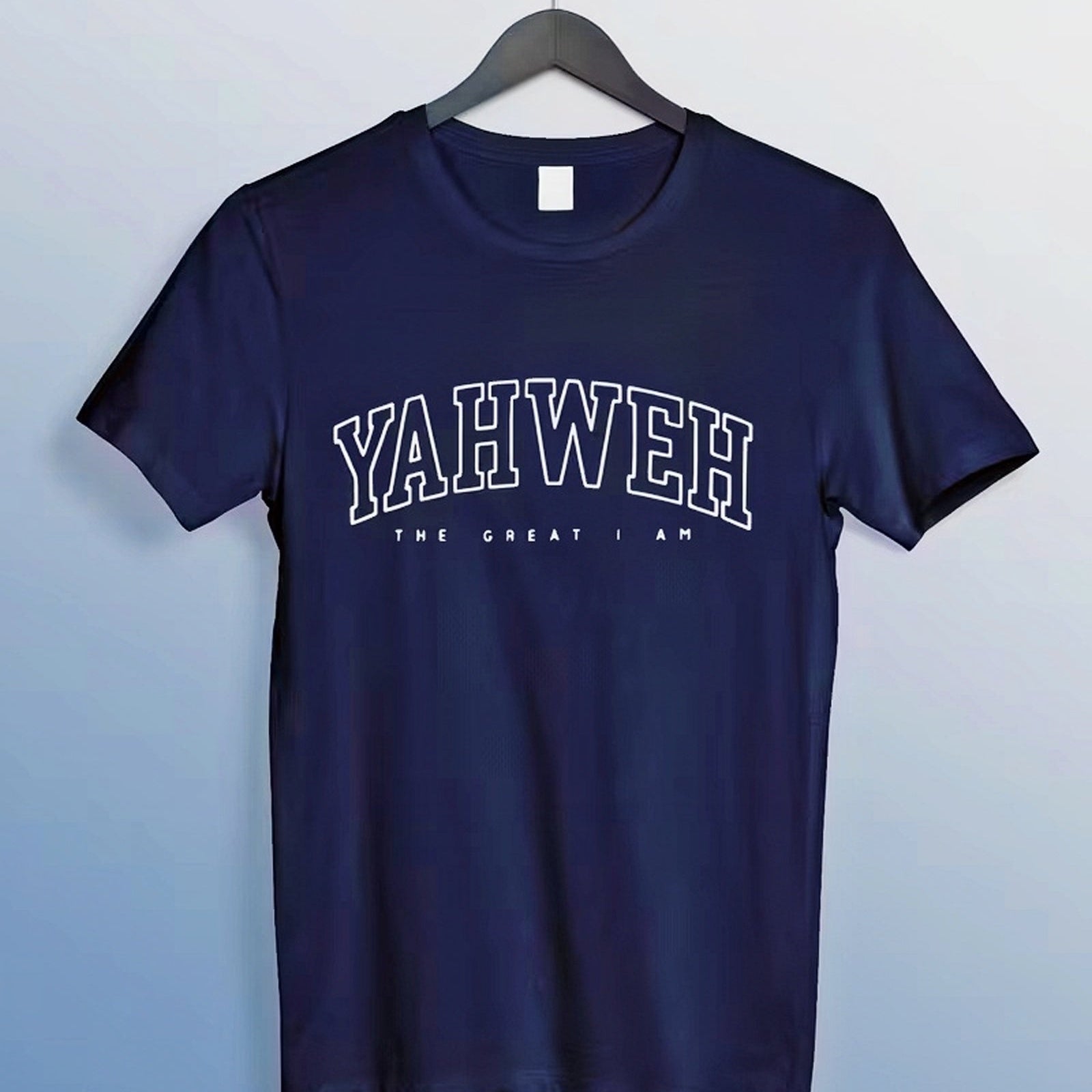 Navy blue t-shirt with 'YAHWEH THE GREAT I AM' text on a hanger against a light blue background