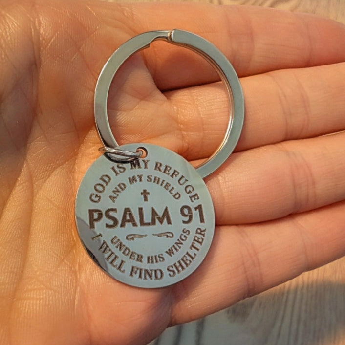 Keychain with 'GOD IS MY REFUGE AND MY SHIELD' and 'PSALM 91' text held in a hand.