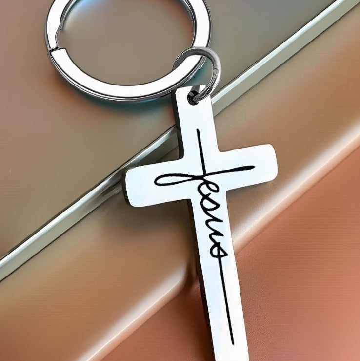 Silver cross keychain with 'Jesus' engraving on a reflective surface